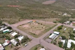 Aerial view of a rectangular park near me, enclosed by roads in a rural area, featuring sparse trees, a few bushes, and a central circular walkway. Nearby RV parks and scattered buildings dot the open grassy fields, with distant hills gracing the clear sky.